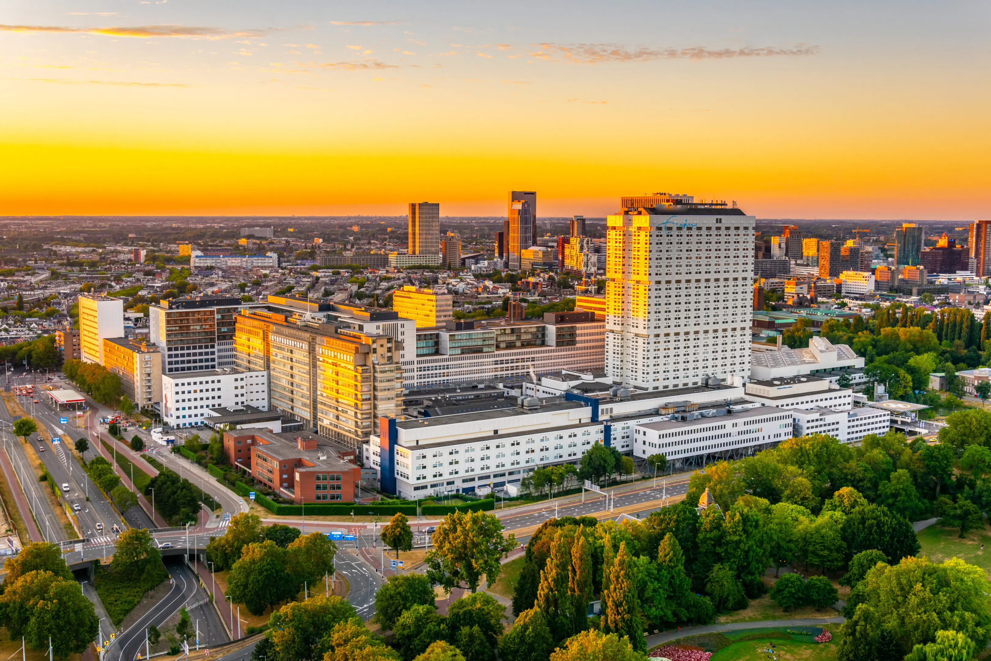 City skyline at sunset with modern buildings and green spaces.