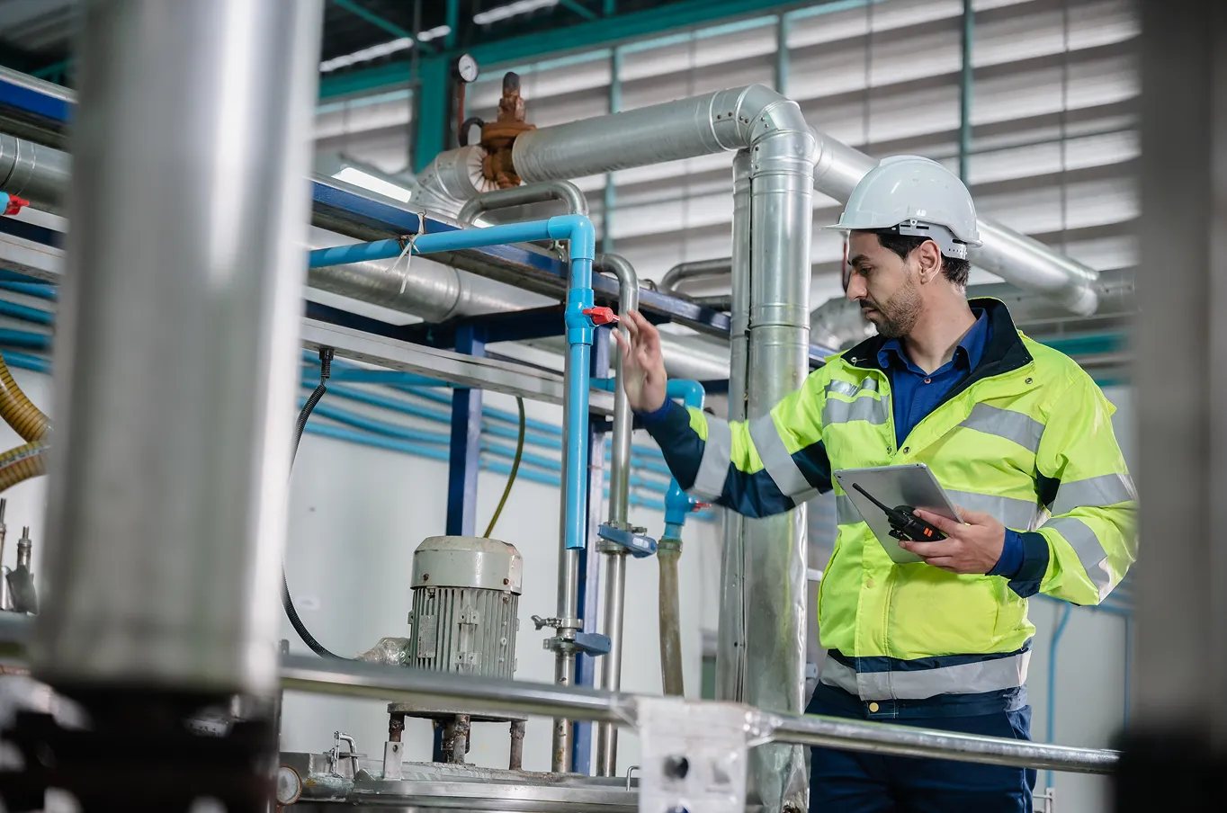 Industrial worker inspecting machinery with tablet.